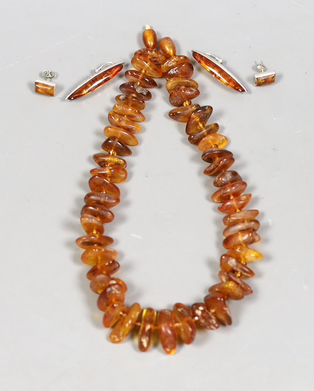 A single strand graduated amber pebble necklace, 42cm and two pairs of white metal mounted amber earrings including 925.